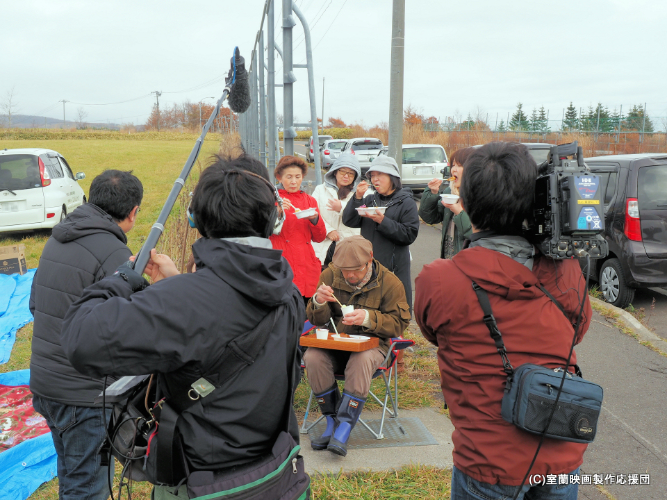 昼食のカレーライスを食べながらインタビューを受ける坪川監督と応援団員
